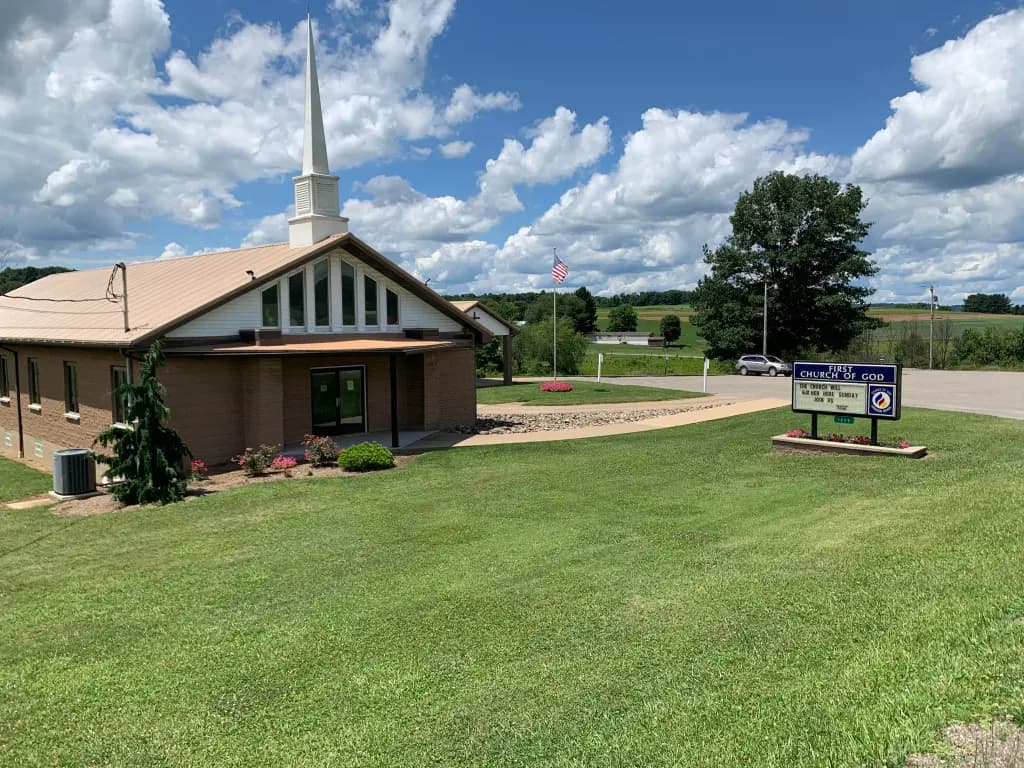 The Dayton First Church of God brick building with white steeple on a green lawn.